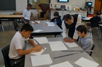 In art, Fr. Ignatius works with the Form IV boys in creating patterns with geometric shapes after studying examples. 